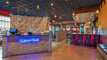 A restaurant interior with a tiled wall, a neon sign, and a bar area.