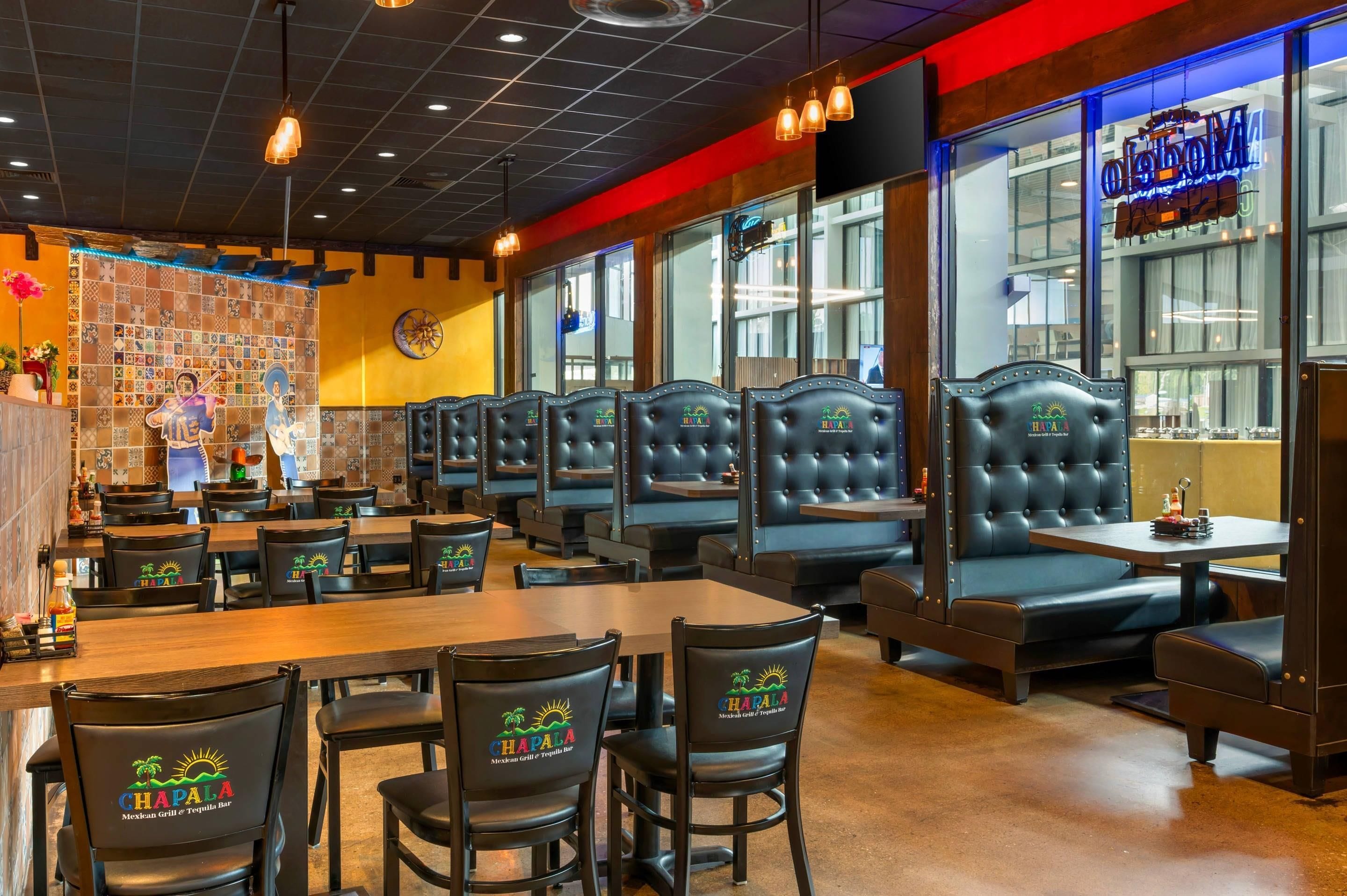 Een restaurantinterieur met zitjes en tafels, met een kleurrijke betegelde muur en een neonbord.