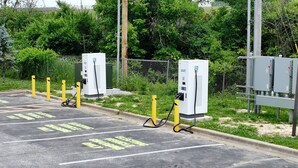 Un espace de stationnement équipé de bornes de recharge pour véhicules électriques, avec des emplacements de stationnement délimités et une clôture en treillis métallique.