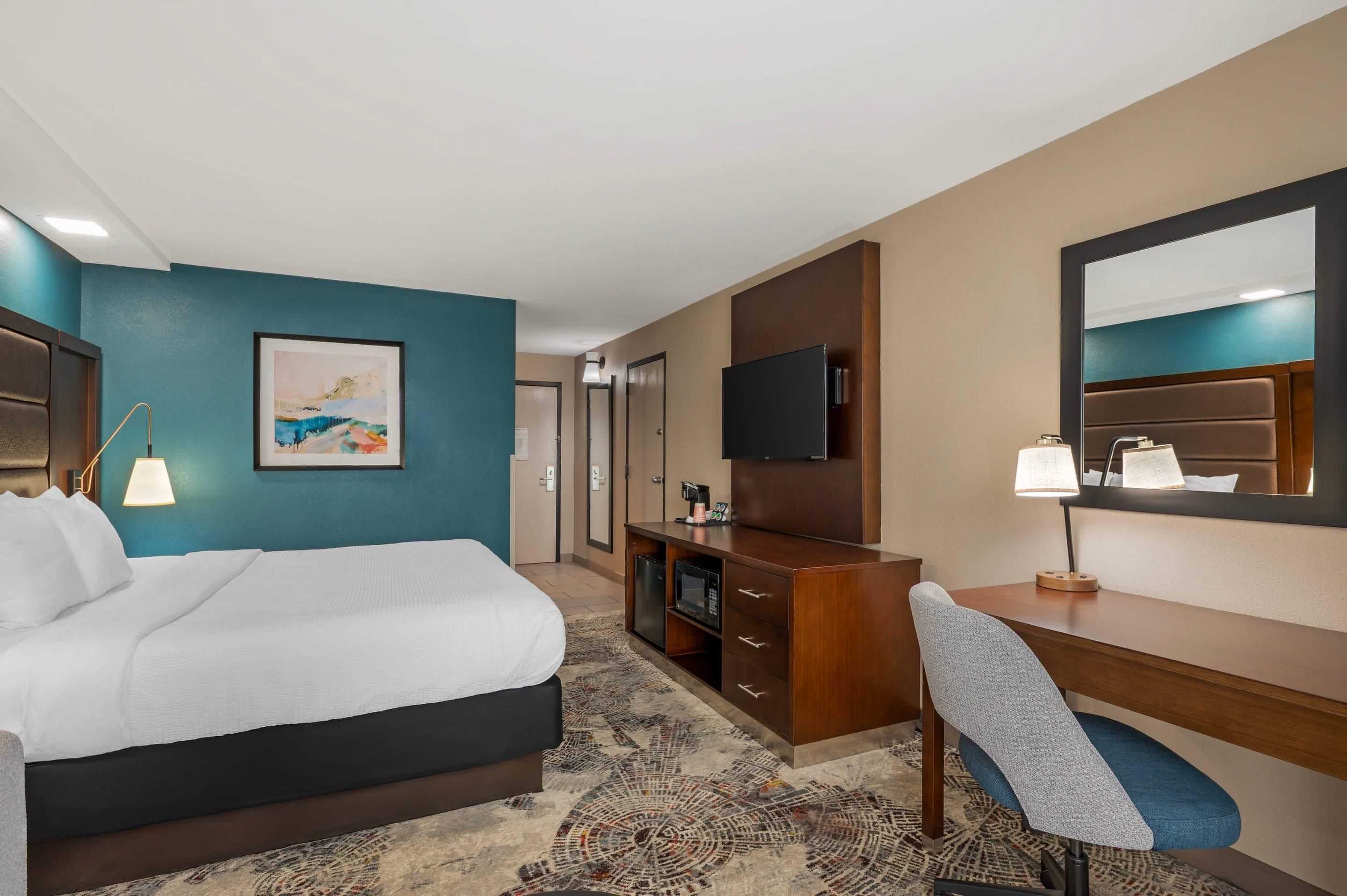 A hotel room with a bed, a desk, a chair, a television, and a painting on the wall.