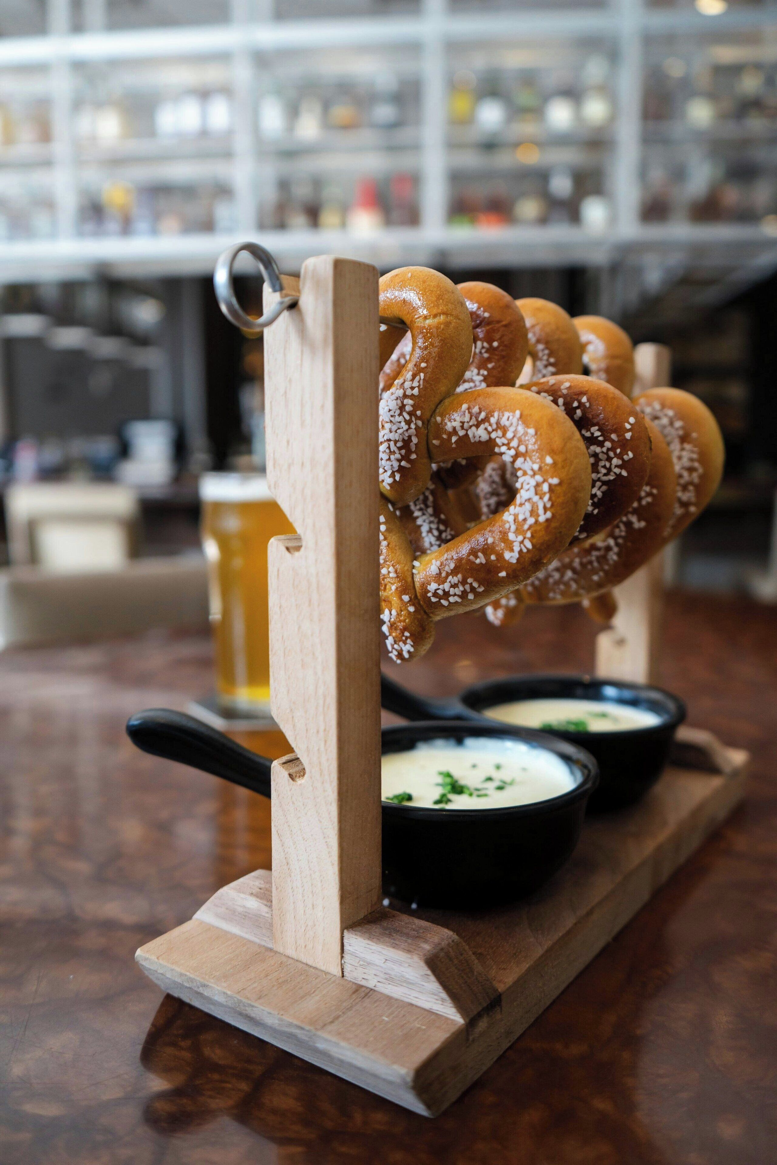 Un présentoir en bois pour bretzels, avec plusieurs bretzels et deux bols noirs contenant de la sauce pour tremper.