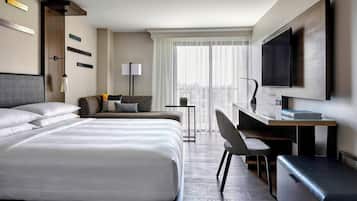 A modern hotel room with a large bed, a desk, a chair, and a TV.