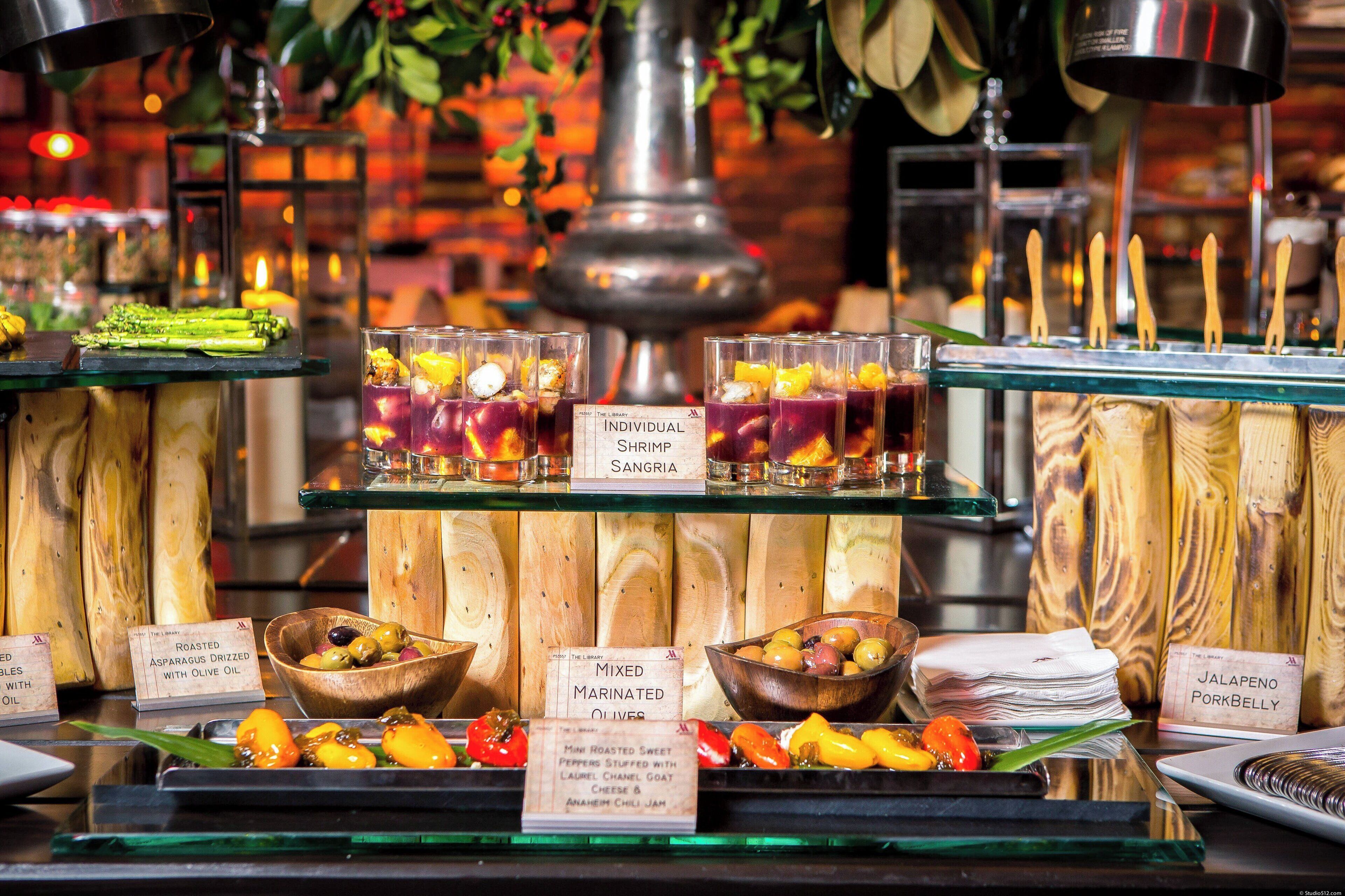 A buffet with various dishes and drinks, including roasted asparagus, mixed marinated olives, and jalapeno pork belly.
