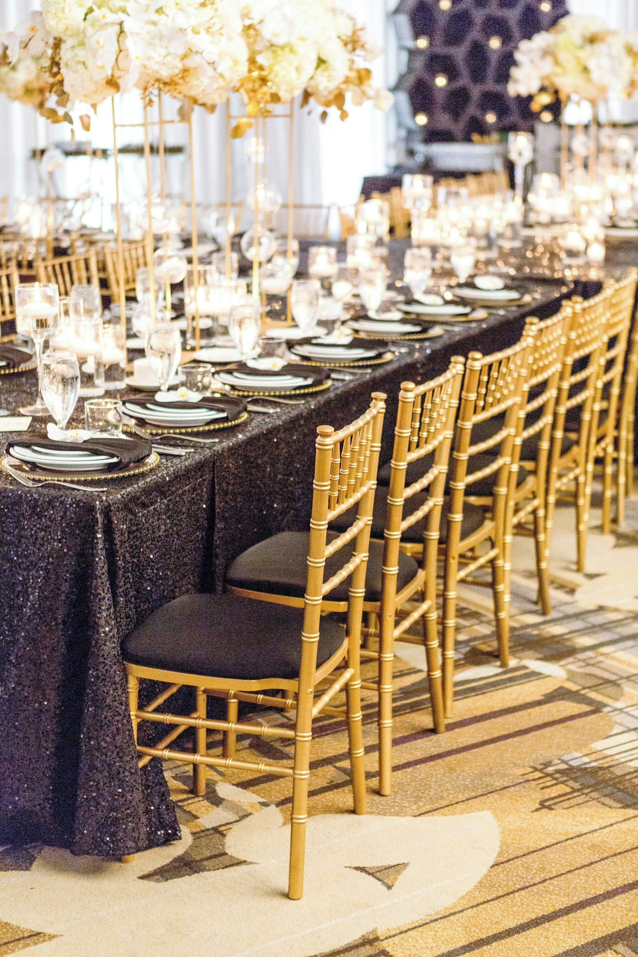 Una larga mesa de banquete con sillas doradas, adornada con flores blancas y cristalería.