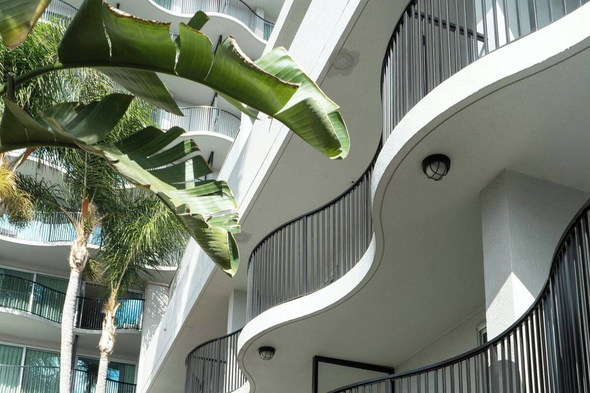 A modern multi-story building with balconies, a well-maintained garden, and outdoor seating.