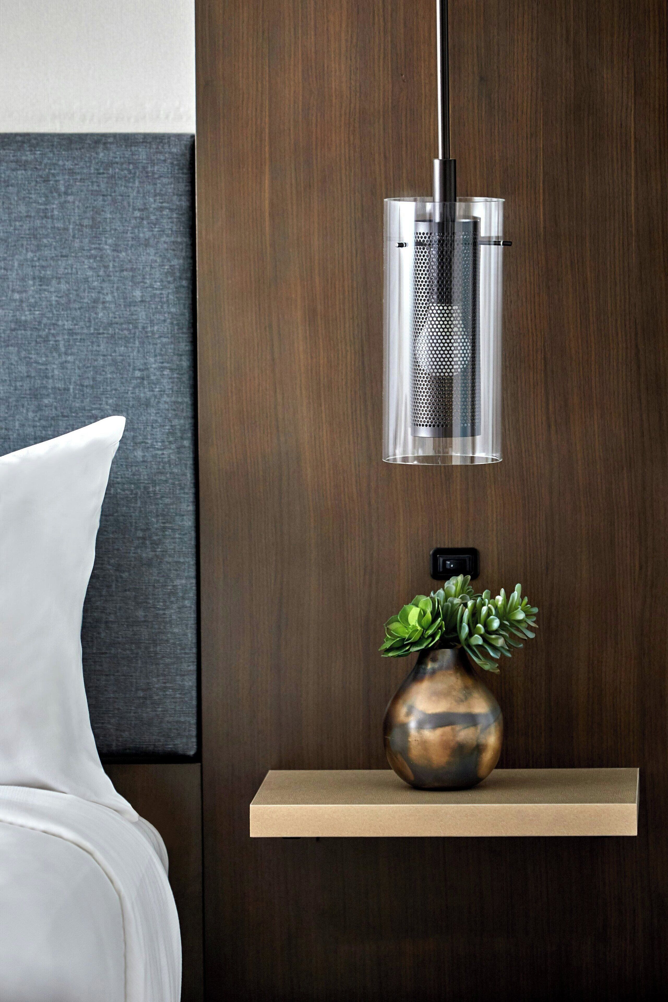 Una habitación moderna con un panel de madera en la pared, una mesita de noche con un jarrón de suculentas y una lámpara colgante.