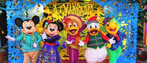 A group of animated characters in front of a festive backdrop with a sign that reads "VIVA UNIDAD".