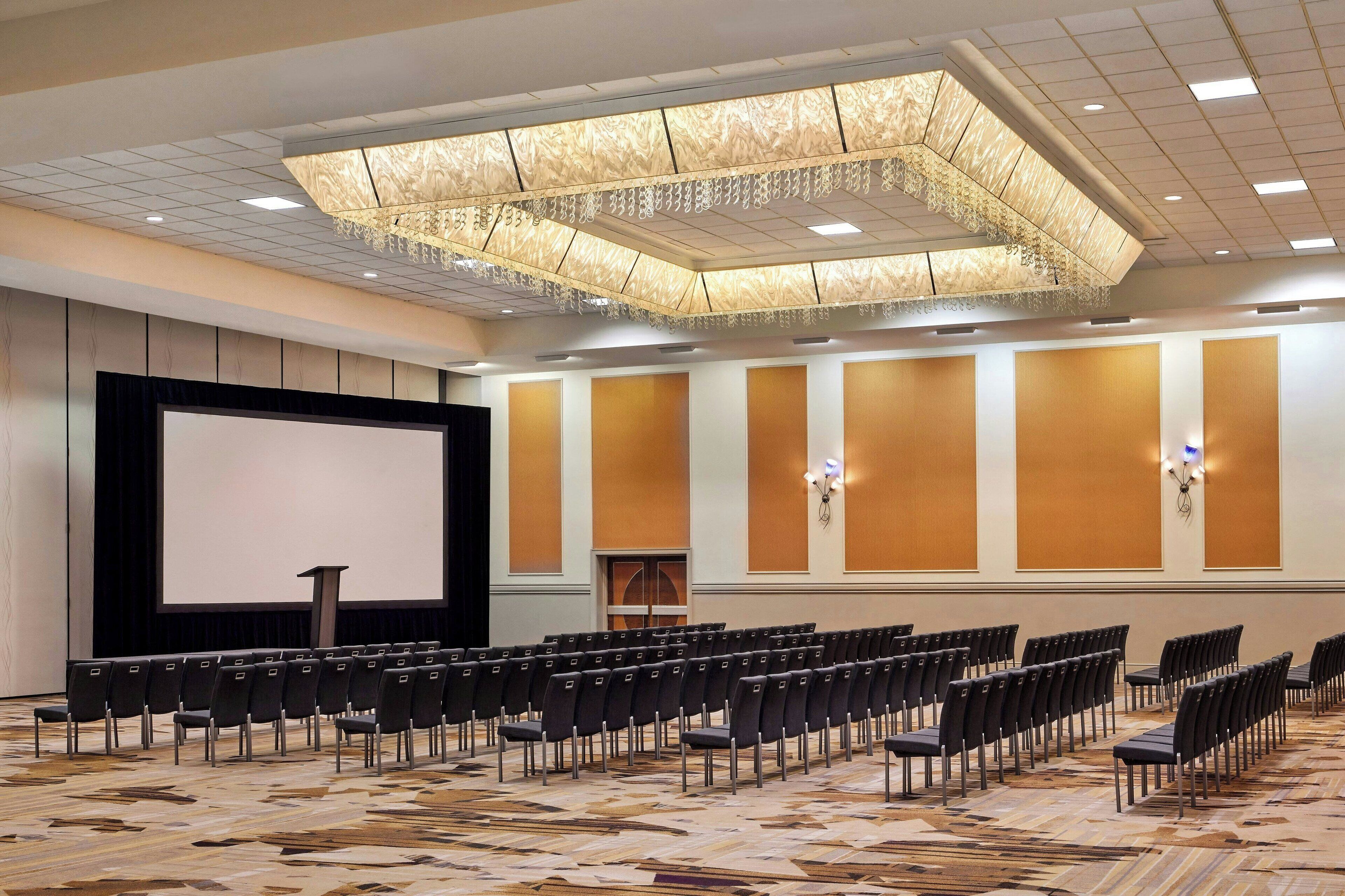 A conference room with rows of chairs, a large screen, and a podium.
