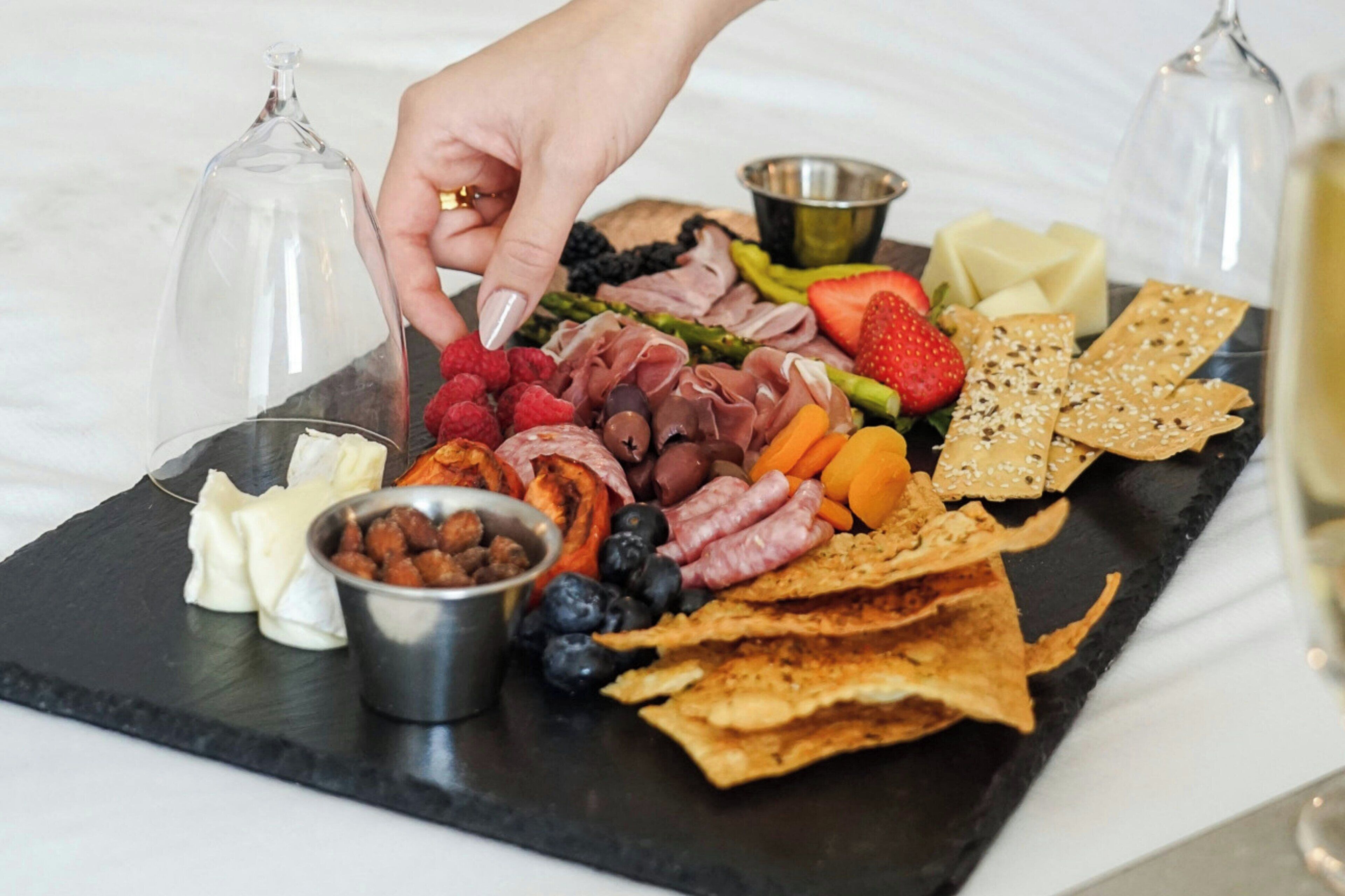 Una tabla de fiambres con diversos quesos, carnes, frutas y galletas.