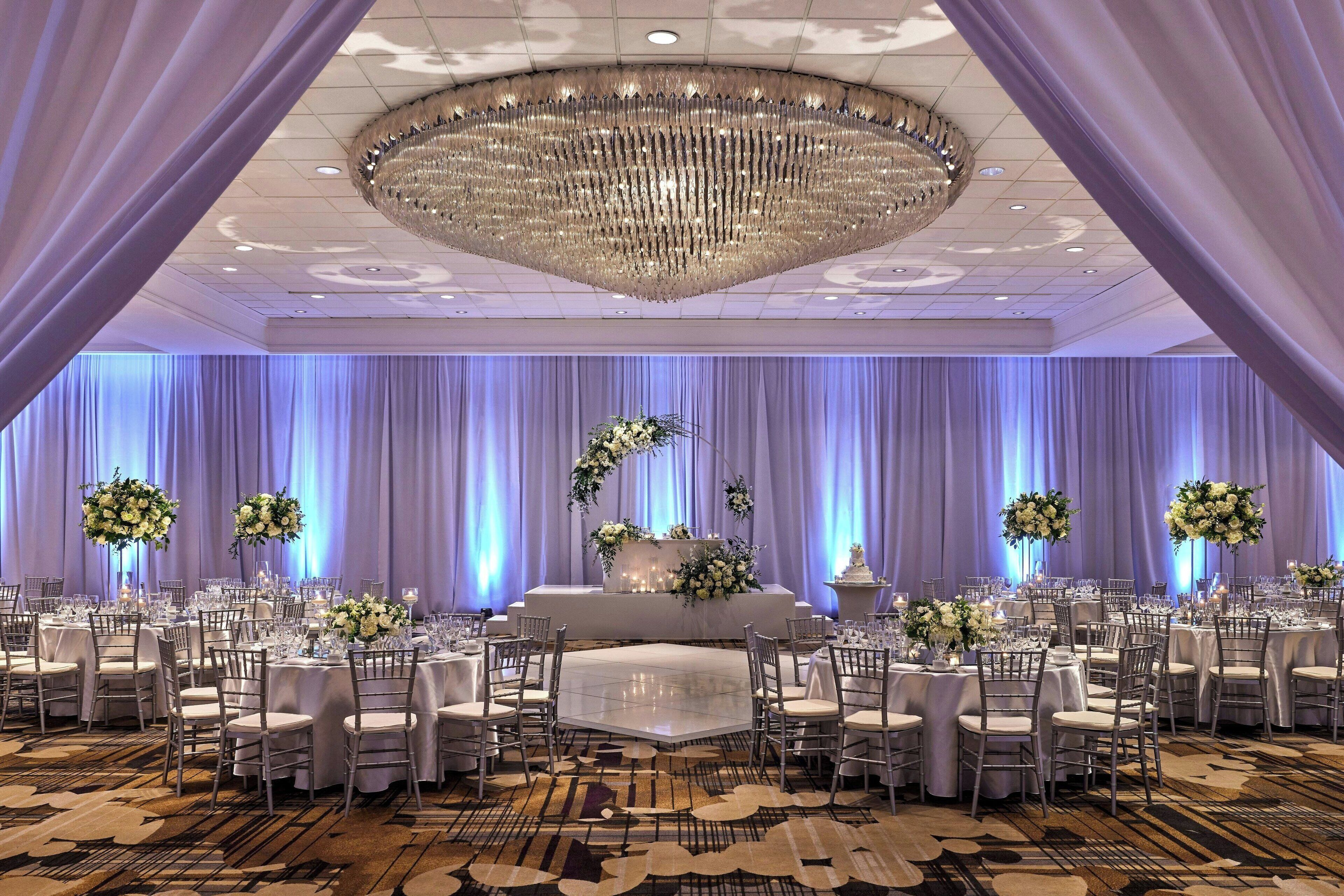 Une salle de banquet avec des tables rondes, des chaises et une composition florale centrale.