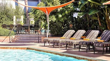 Una piscina al aire libre, sombrillas, sillones reclinables de piscina