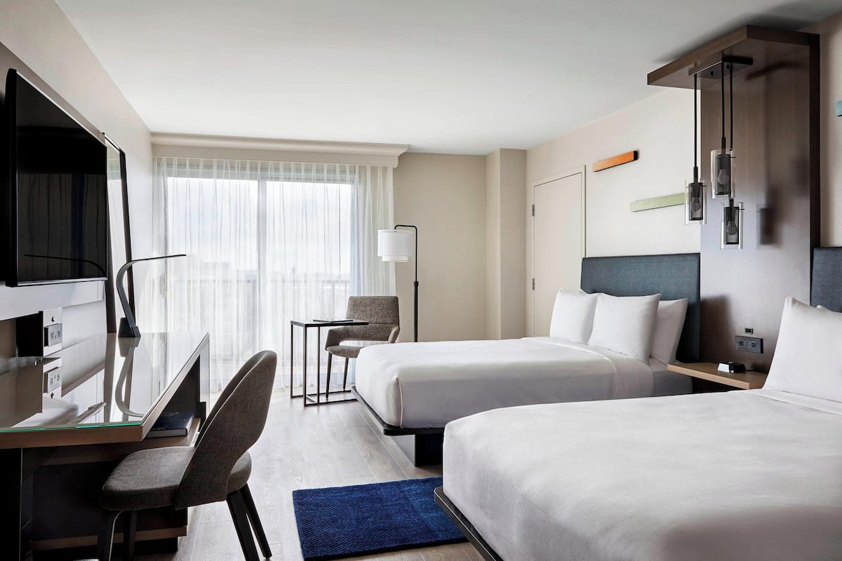 A hotel room with two beds, a desk with a chair, a TV, and a window with curtains.