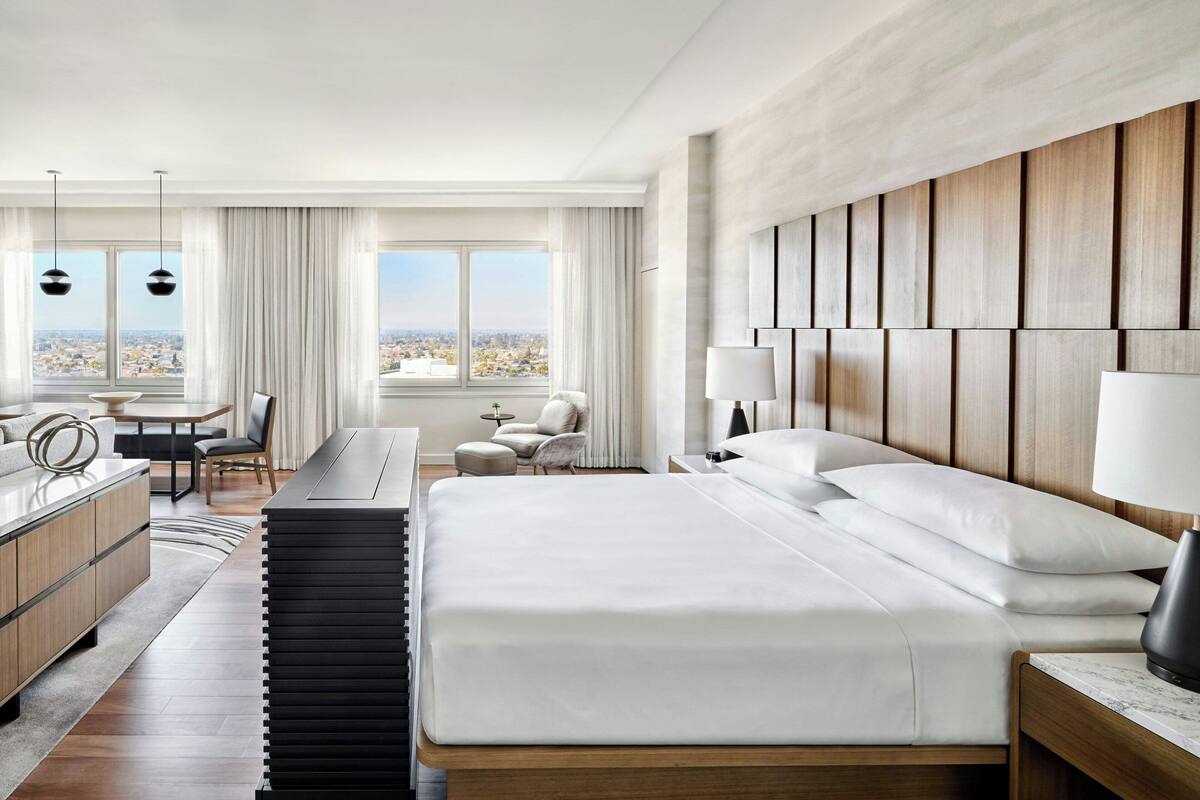 A modern hotel room with a large bed, a desk, a chair, and a view of the city.