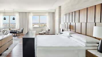 A modern hotel room with a large bed, a desk, a chair, and a view of the city.
