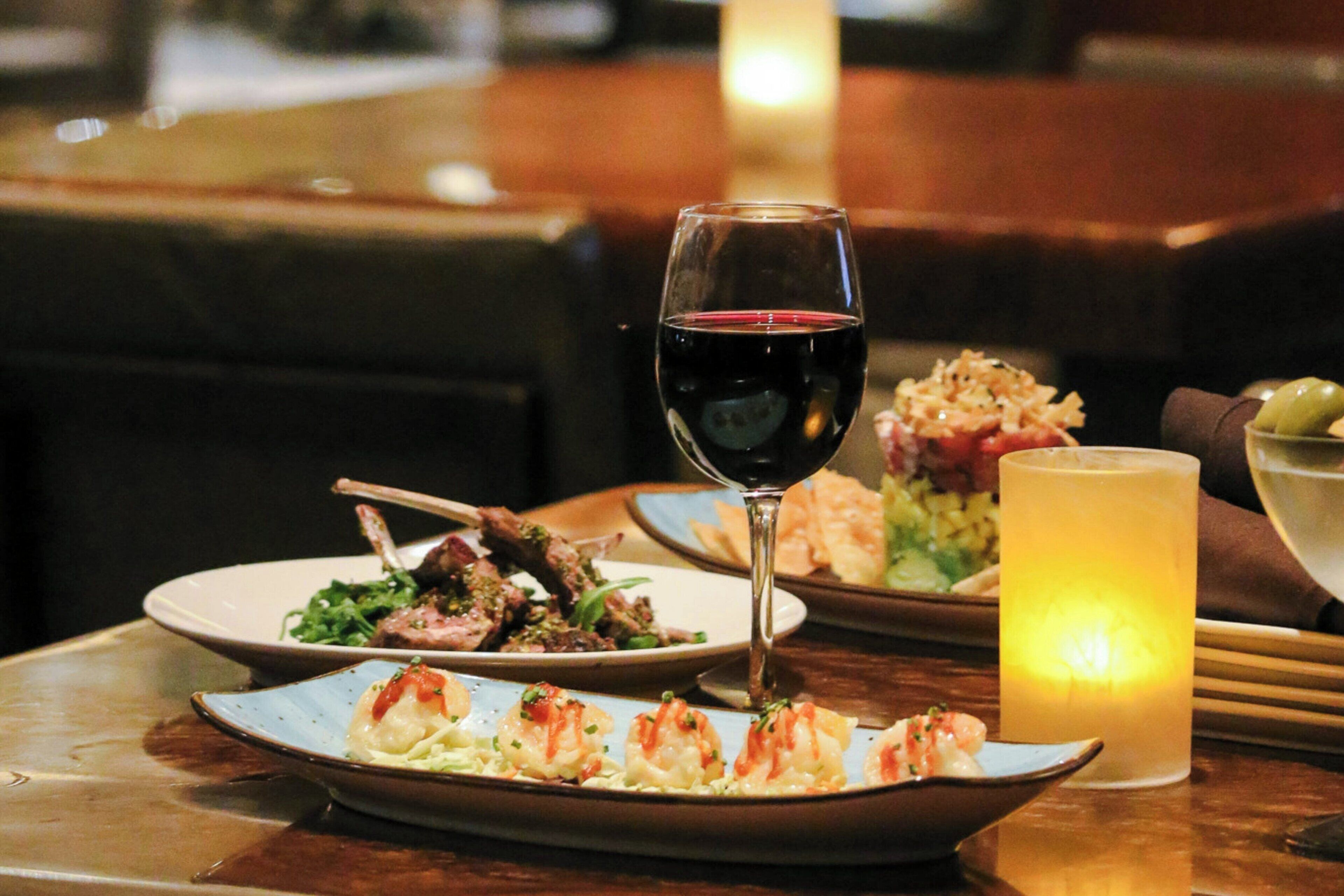A dining table with plates of food, a glass of red wine, and a candle.