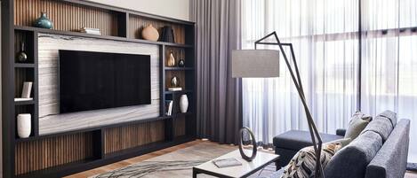 A modern living room with a large flat-screen TV, a sofa, a coffee table, and a floor lamp.