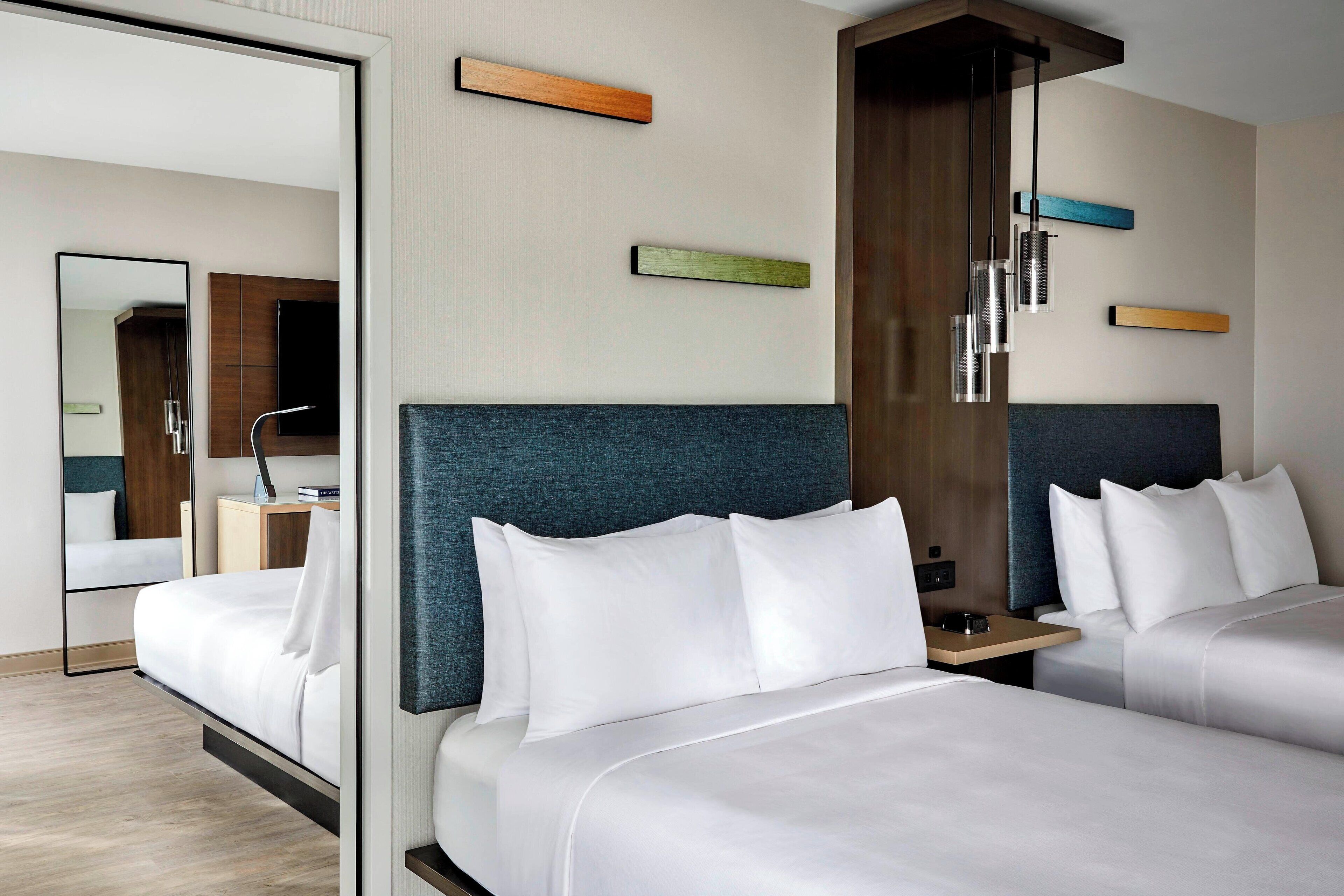 A hotel room with two beds, a large mirror, and a wooden wardrobe.