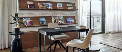A modern dining area with a wooden table, two chairs, a potted plant, and a bookshelf with travel books.
