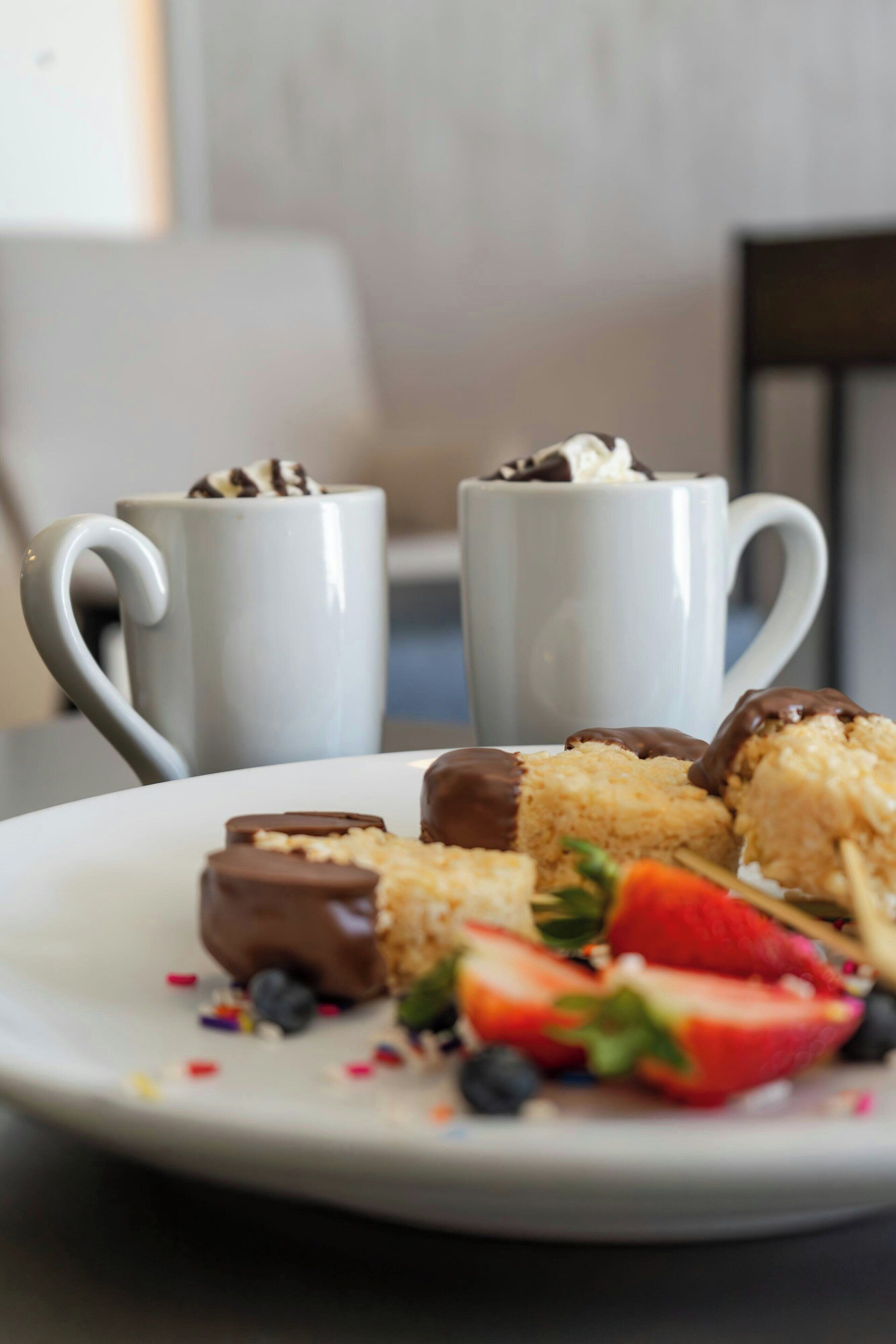 Une assiette de desserts comprenant des fraises et des douceurs enrobées de chocolat, accompagnée de deux tasses blanches.