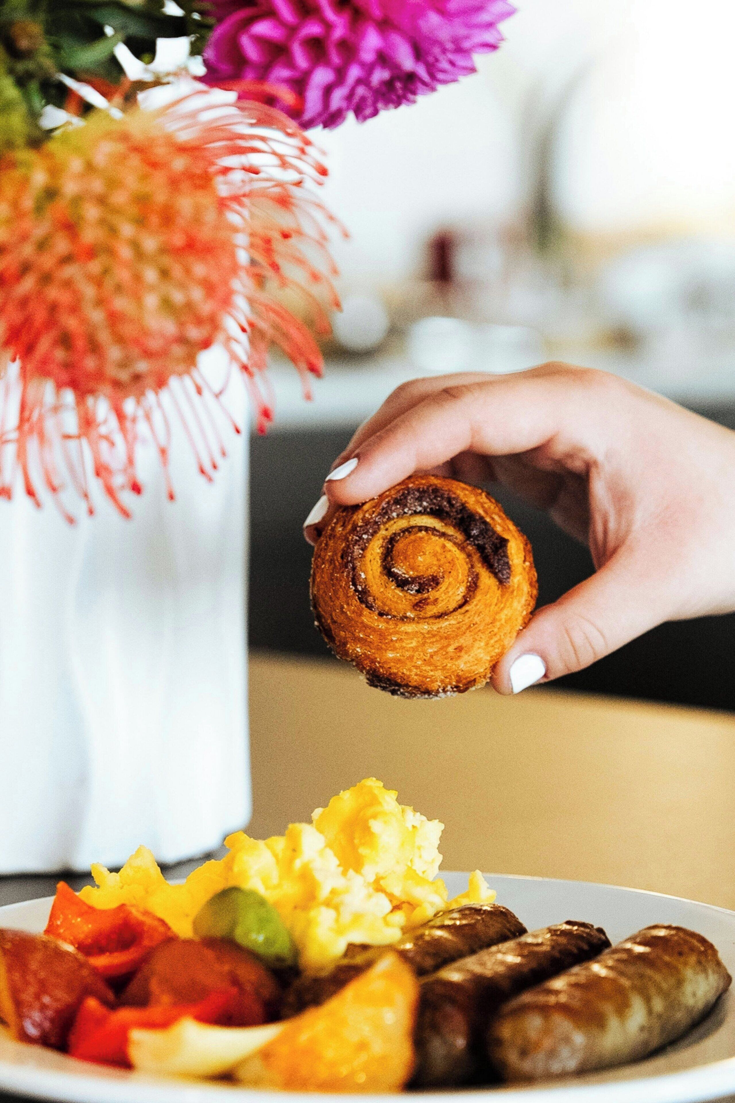 A plate of food including sausages, scrambled eggs, and a cinnamon roll.