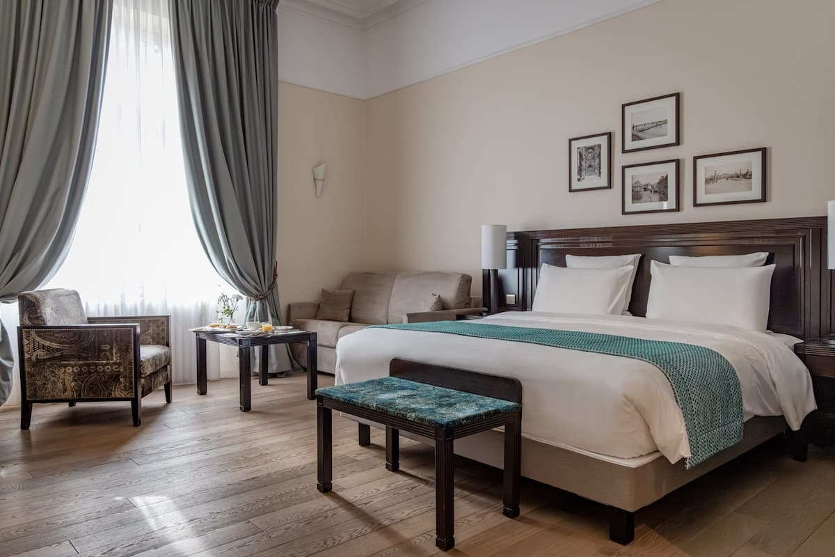 Quarto de hotel com cama, cadeira, mesa pequena e um banco.