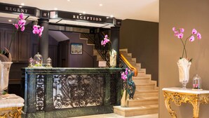 A reception area with a marble counter, ornate gold and black furniture, and pink orchids. - Hôtel Régent Contades  By Stay Collection (Strasbourg)