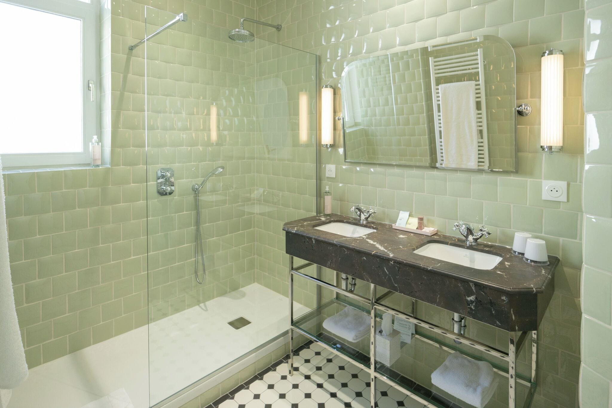 A bathroom with a glass-enclosed shower, a double sink with a marble countertop, and a mirror with a towel rack.