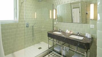 A bathroom with a glass-enclosed shower, a double sink with a marble countertop, and a mirror with a towel rack.