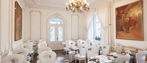 Un comedor formal con sillas, mesas y candelabro blancos.