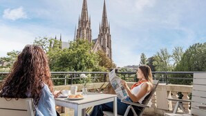 Two people seated at a table with a newspaper, overlooking a cathedral with two spires. - Hôtel Régent Contades  By Stay Collection (Strasbourg)