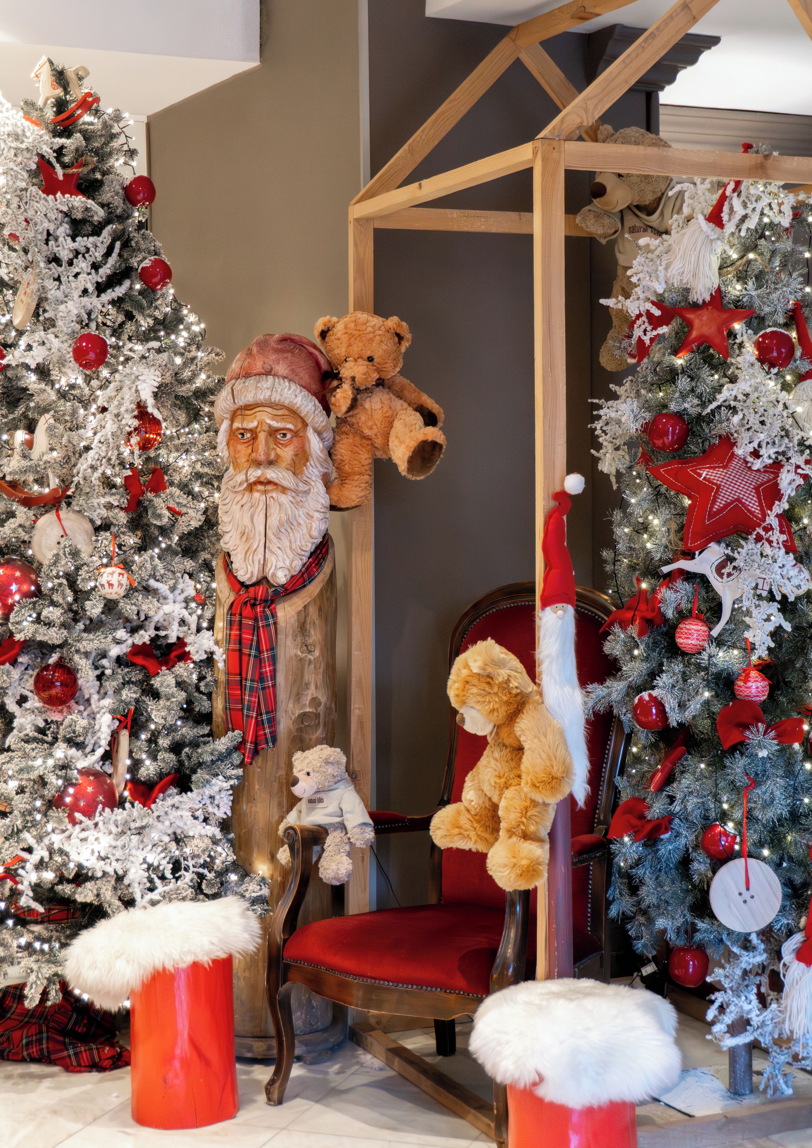 A room with two Christmas trees, a wooden chair, and a teddy bear.