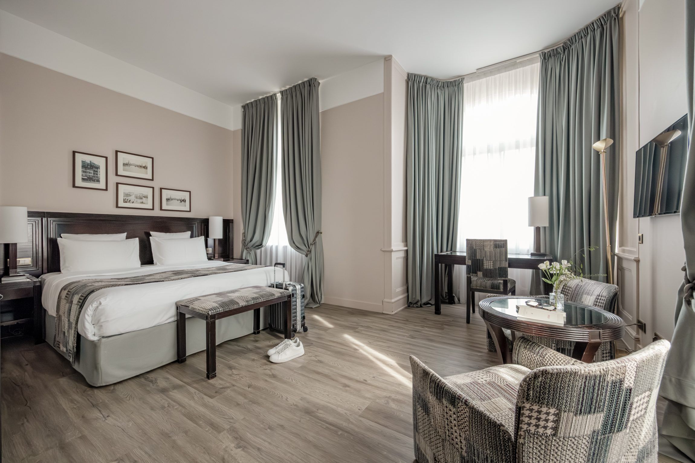 Quarto de hotel com cama, mesas de cabeceira, escrivaninha, cadeira e vista para o exterior.