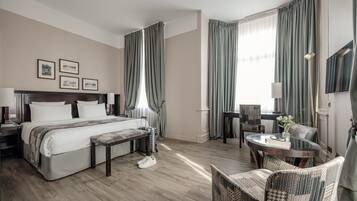 Quarto de hotel com cama, mesas de cabeceira, escrivaninha, cadeira e vista para o exterior.