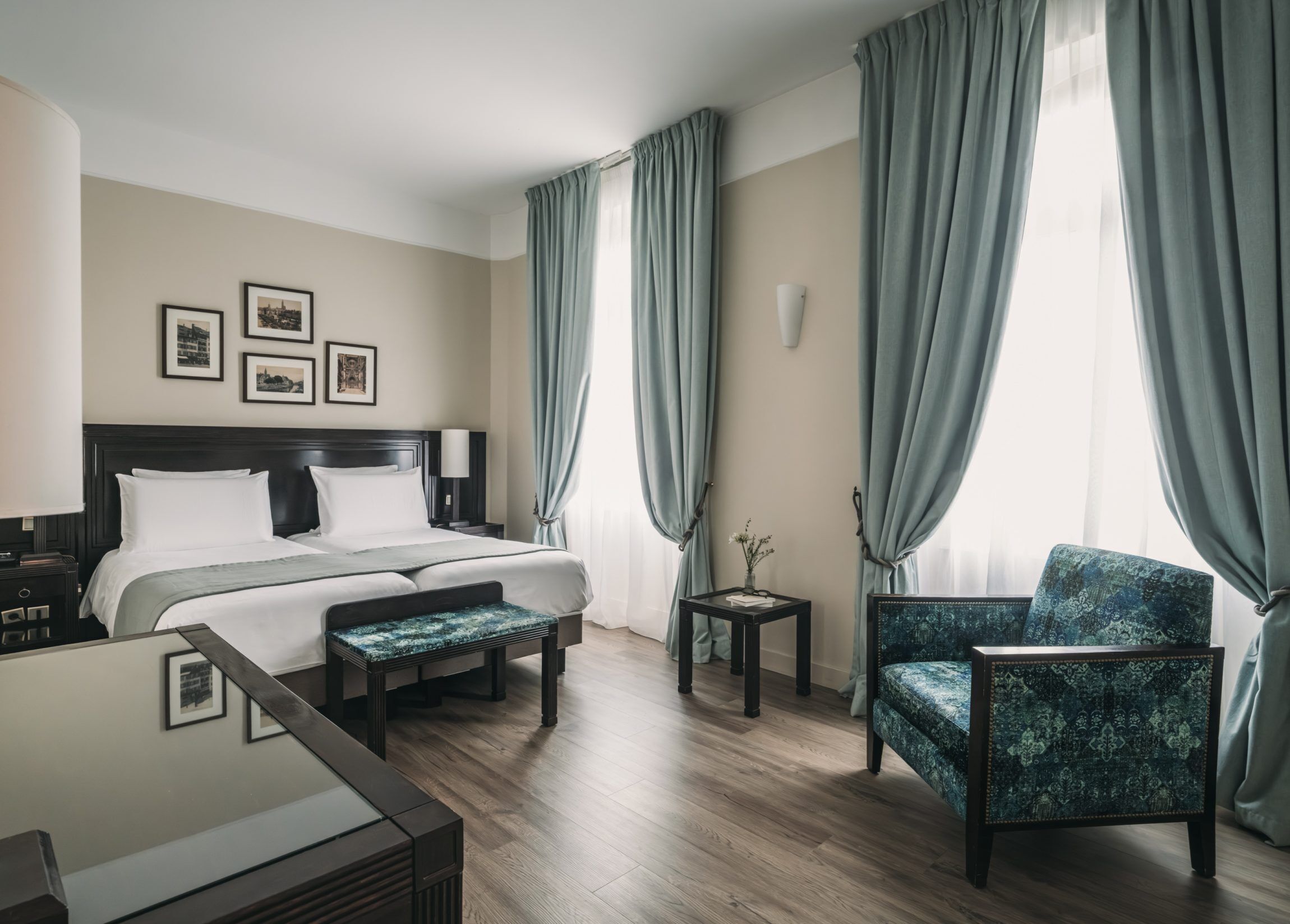 Une chambre d’hôtel avec un lit, une chaise, une petite table et un cadre avec une image accroché au mur.