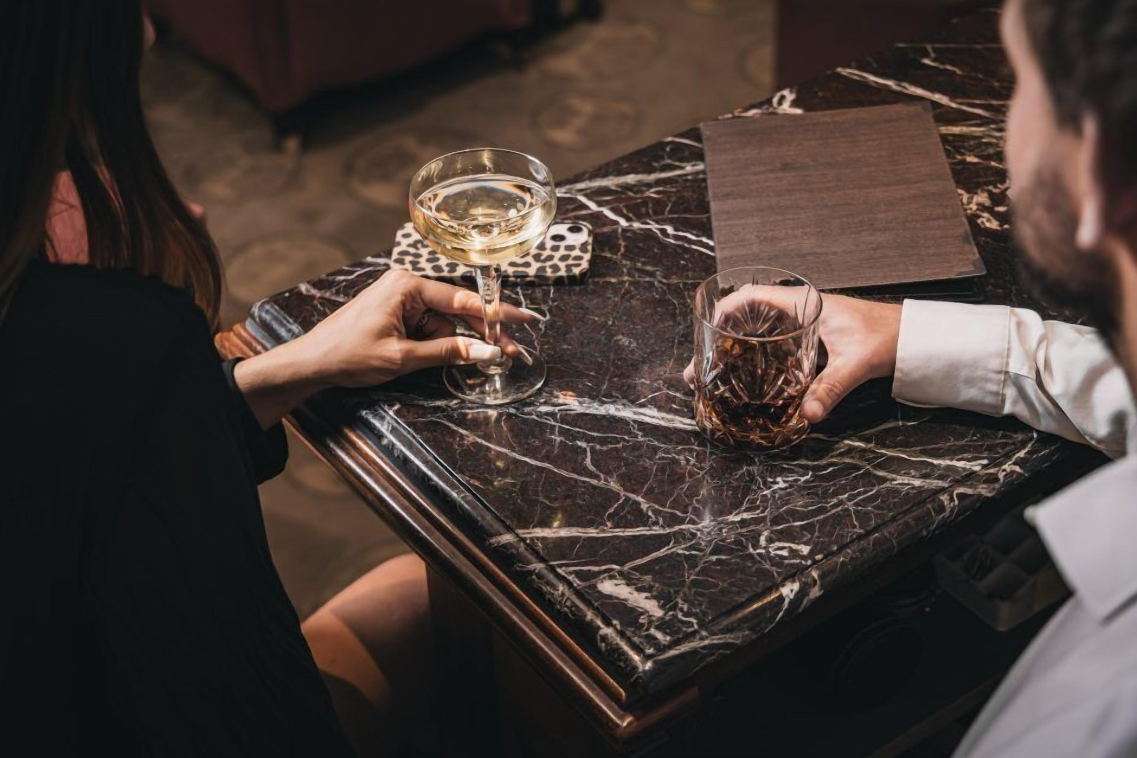 Una mesa de mármol con dos vasos de bebidas, uno transparente y otro de color ámbar, y una base de madera.