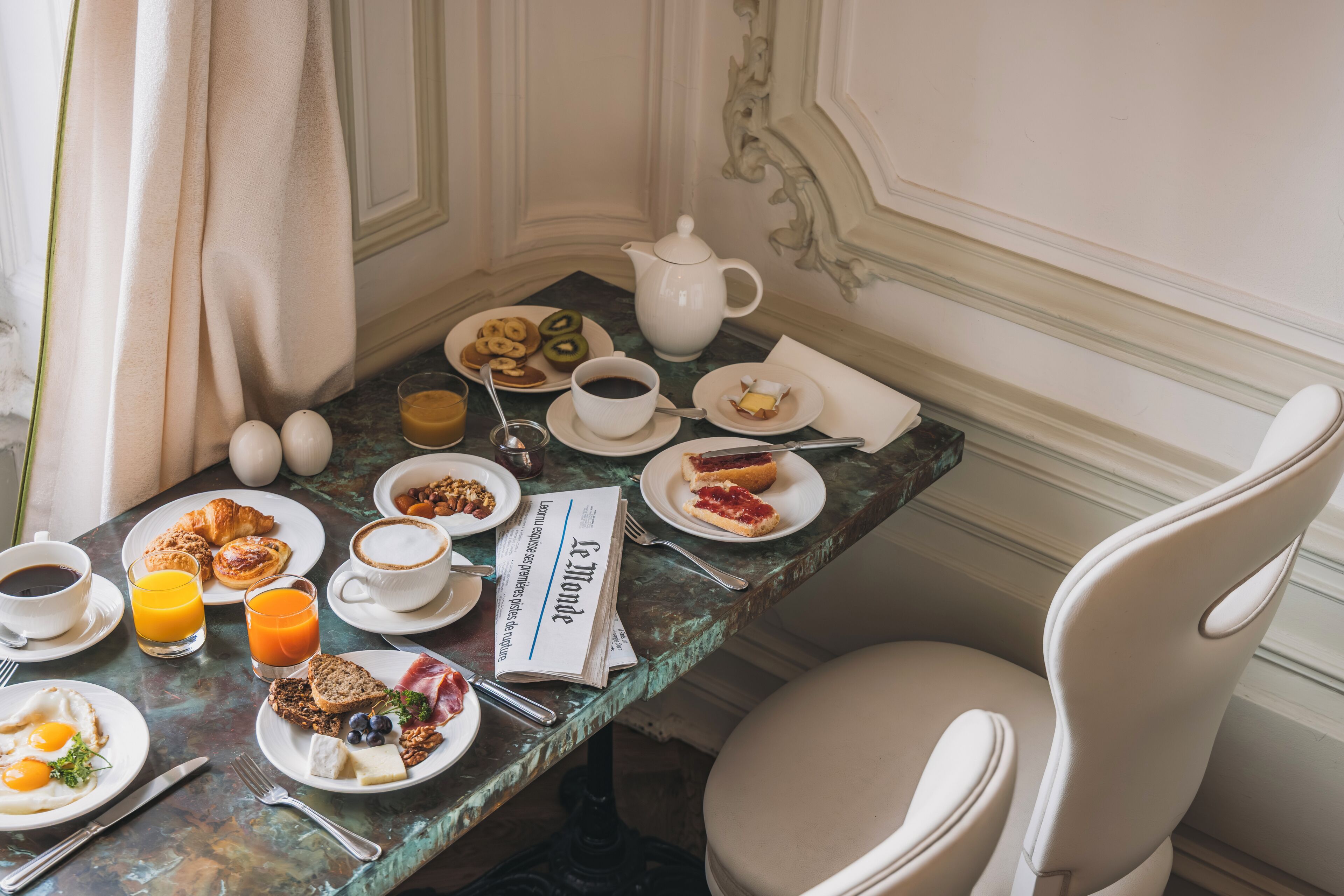 Una mesa de desayuno con diferentes alimentos, un periódico y una tetera.