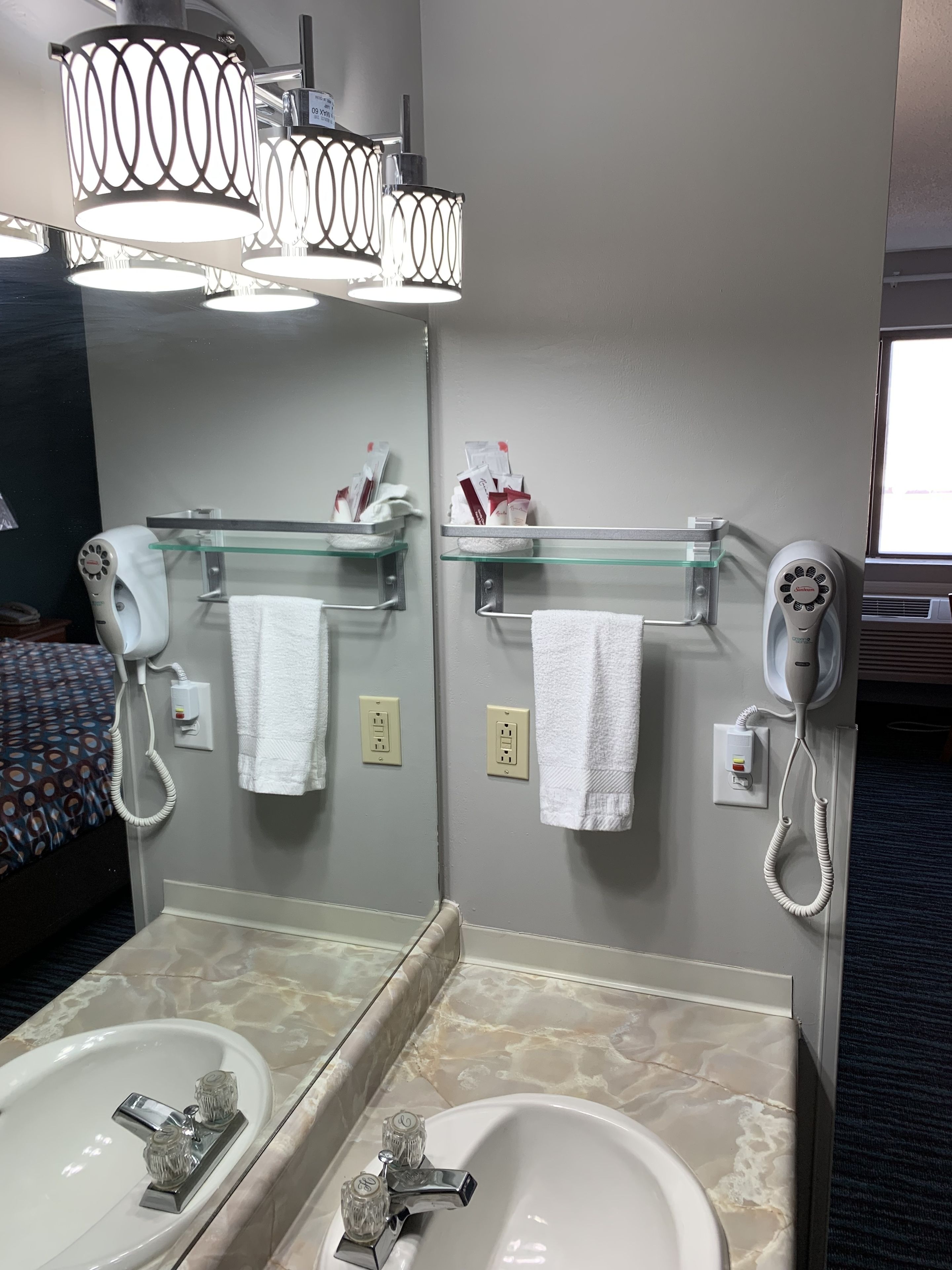 A hotel bathroom with two sinks, a mirror, a hairdryer, and a towel rack.