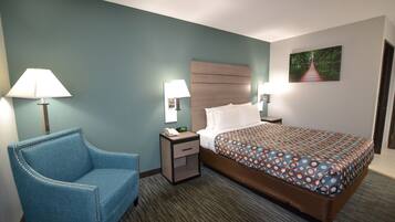 A hotel room with a bed, a chair, a nightstand, and a lamp.