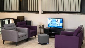 A living room with four purple and grey sofas, a flat-screen TV, and a small side table.