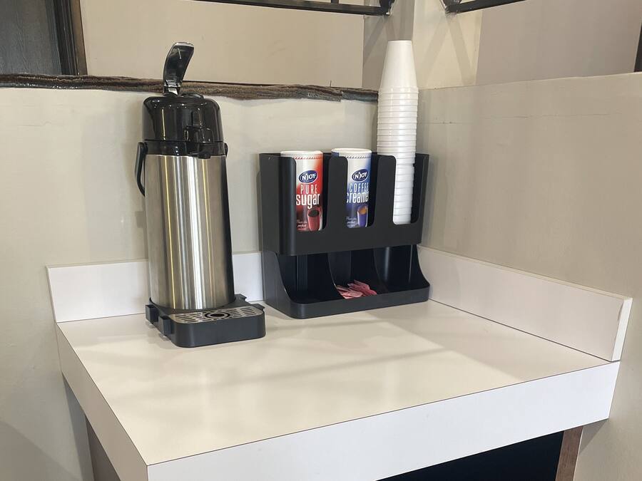 A kitchen counter with a coffee maker, a coffee dispenser, and a cup holder.