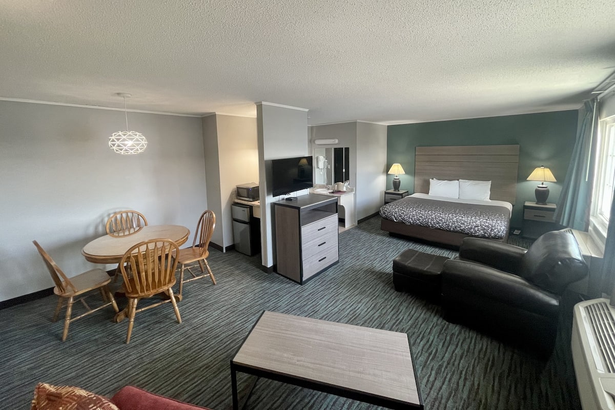 Ein Hotelzimmer mit Bett, Schreibtisch mit Computer, Fernseher, Essbereich mit Stühlen und einer Couch.