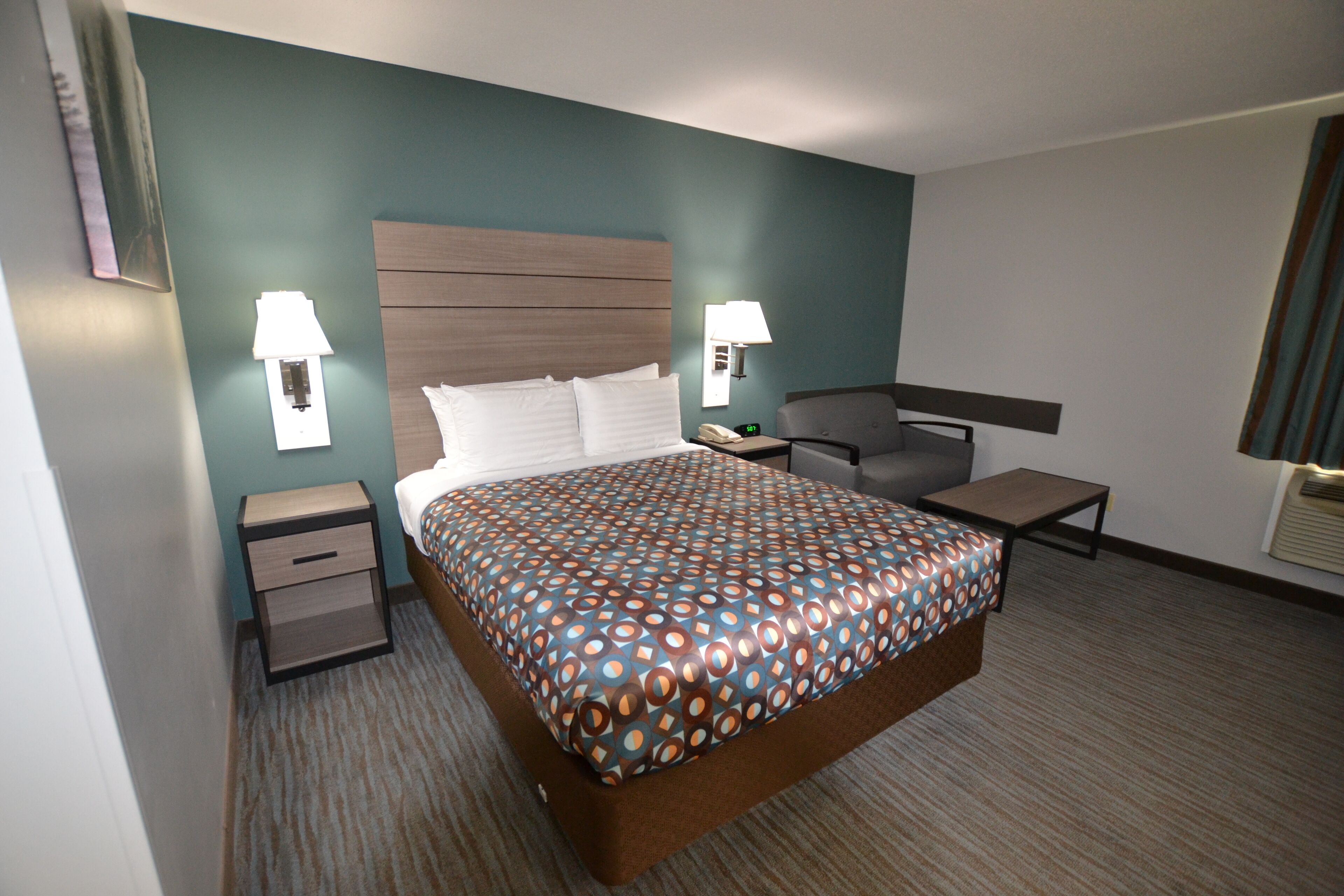 A hotel room with a large bed, two bedside tables, a chair, and two wall-mounted lamps.