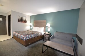 A hotel room with a bed, bedside table, lamp, and a sofa. - Countryside Inn & Suites (Council Bluffs)