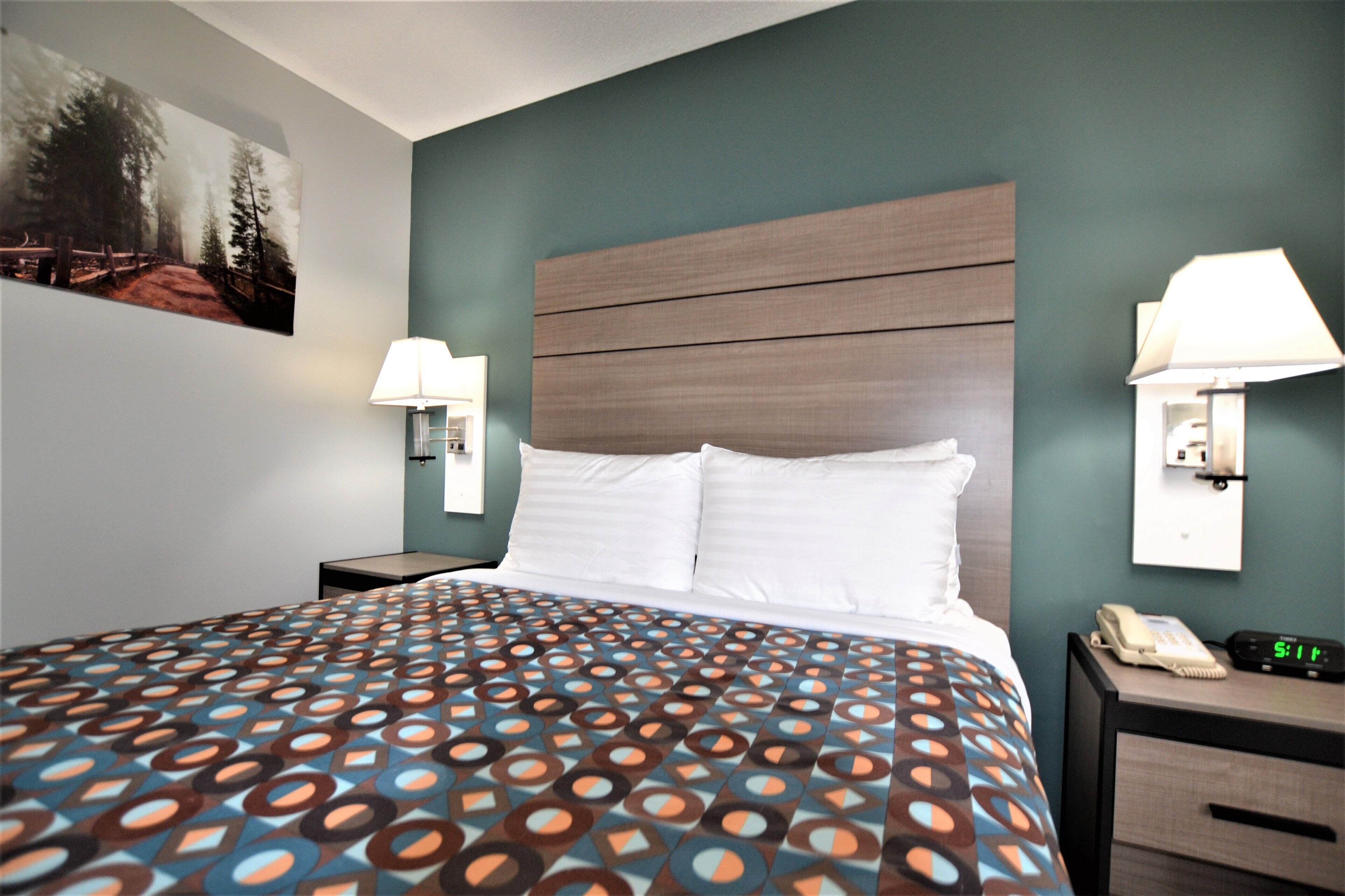 Une chambre d’hôtel avec un grand lit, deux tables de chevet, une petite table avec une lampe, un téléphone fixé au mur et un tableau accroché au mur.