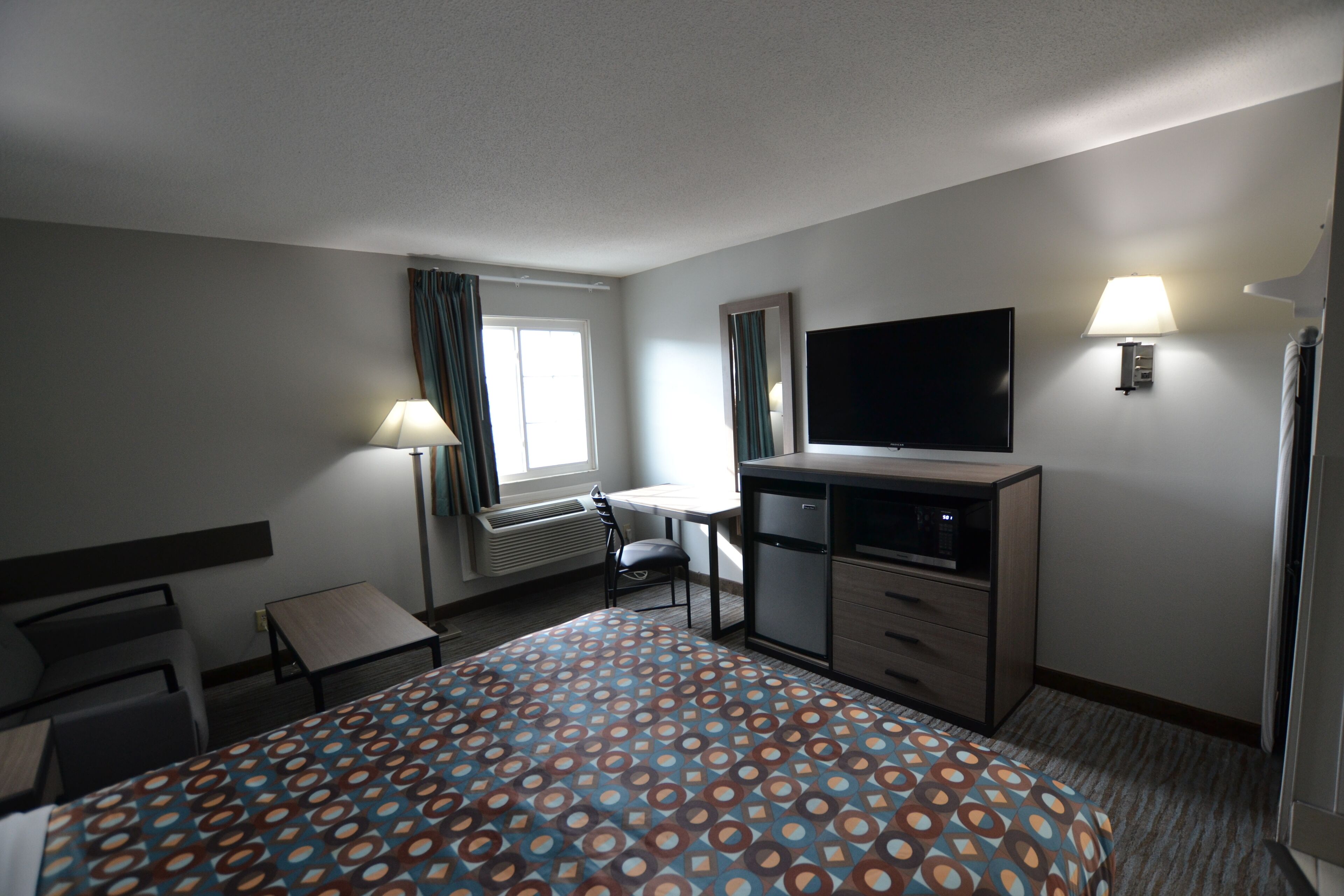 A hotel room with a bed, desk, chair, TV, and a window with curtains.