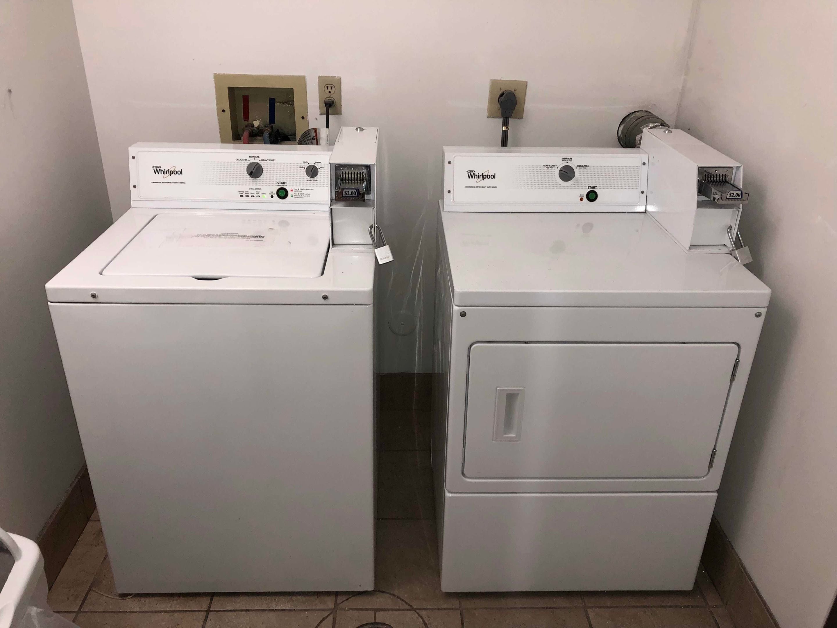 Dos lavadoras Whirlpool de carga frontal en un lavadero con piso de baldosas y una ventana pequeña.