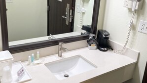 A hotel bathroom with a sink, mirror, hair dryer, and coffee maker.