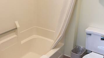 A bathroom with a bathtub, toilet, and a trash can.