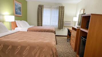 A hotel room with two beds, a desk, a chair, a television, and a window with curtains.