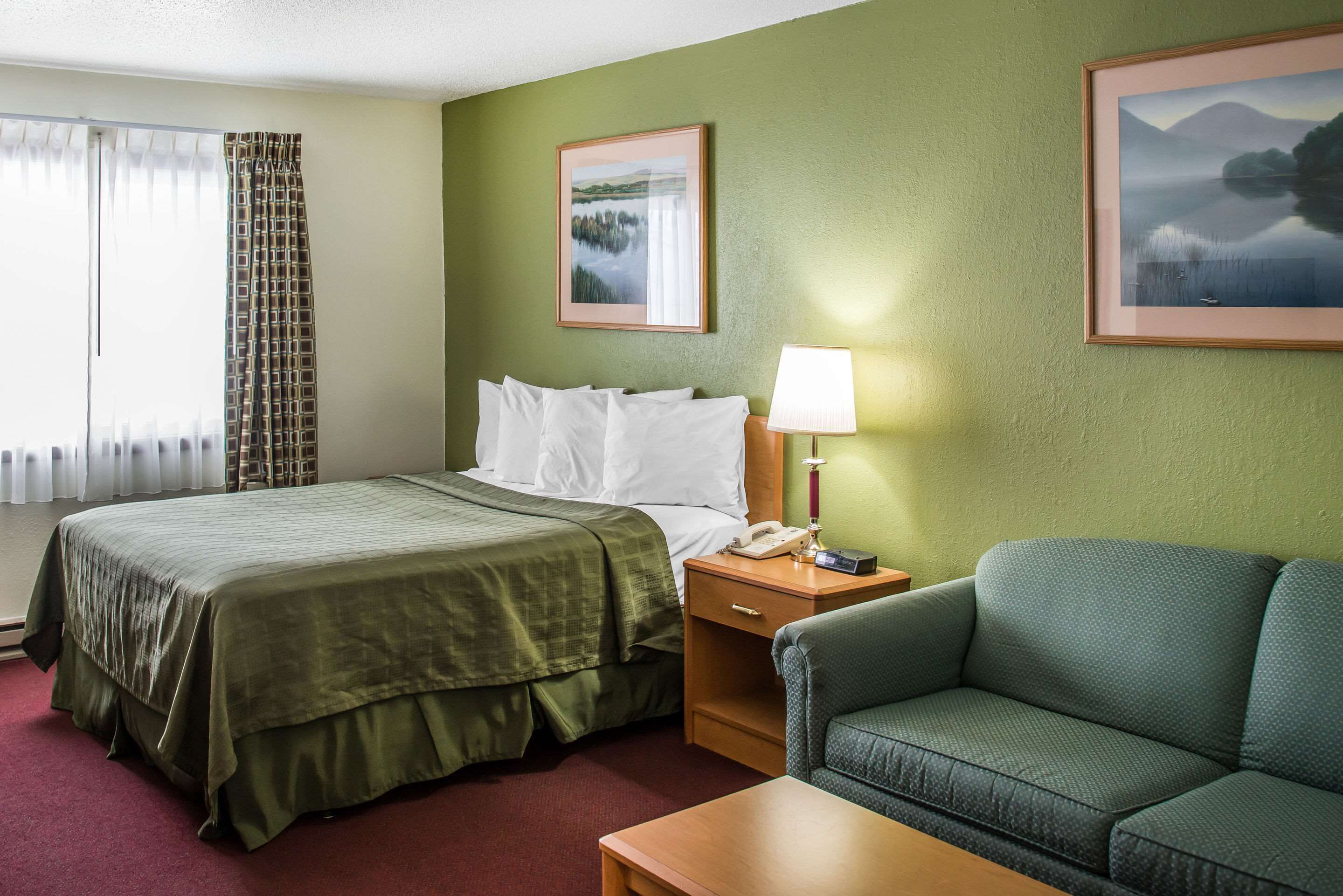 A hotel room with a bed, a nightstand with a lamp, a sofa, and two framed pictures on the wall.